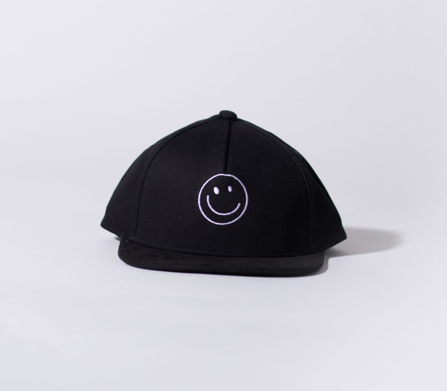 A black snapback by rad toddler. The front has a smiley face on it and Comes in different sizes and looks very stylish