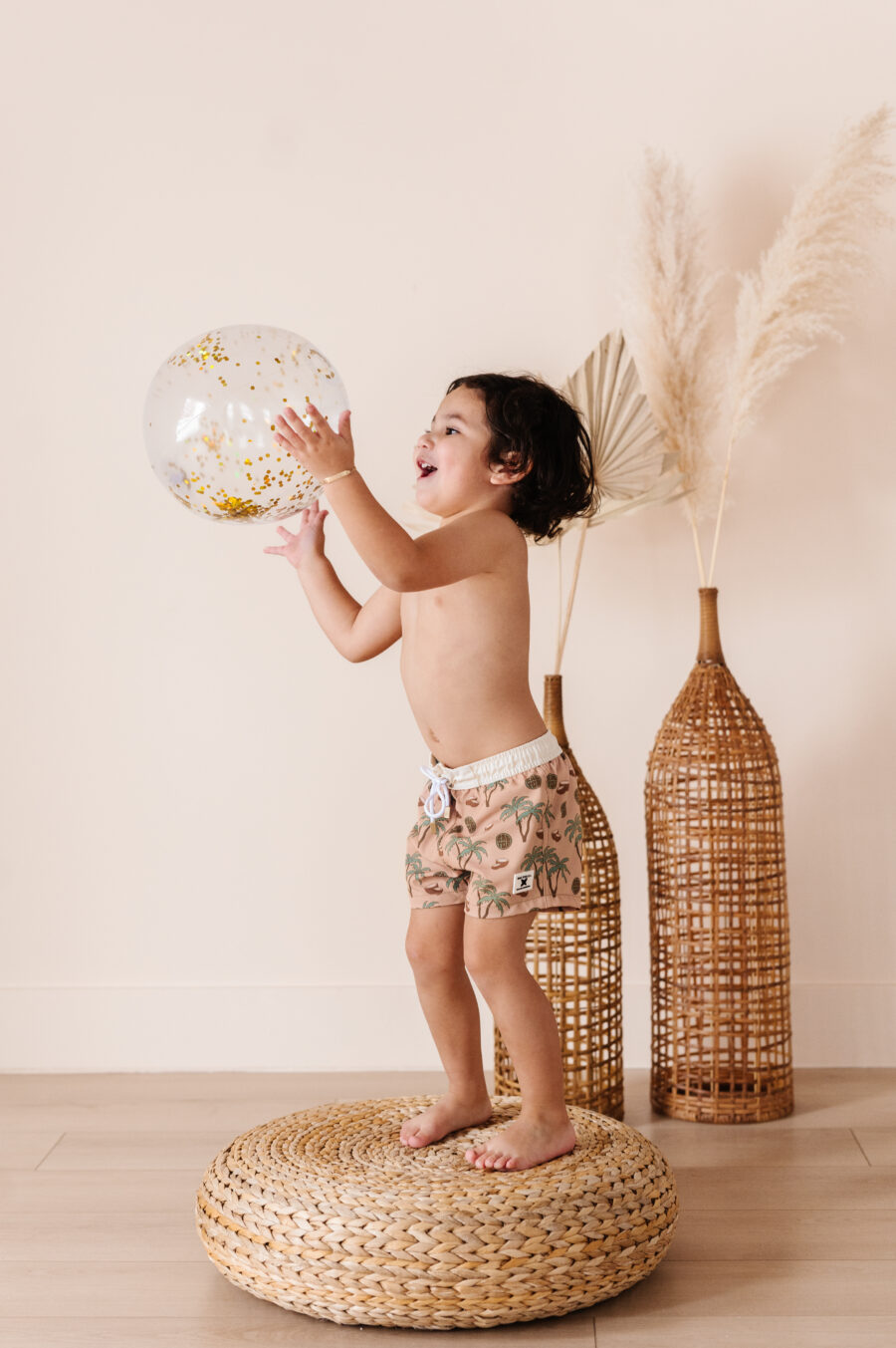 boy is happily playing with a balloon while wearing palm tree shorts by Rad Toddler