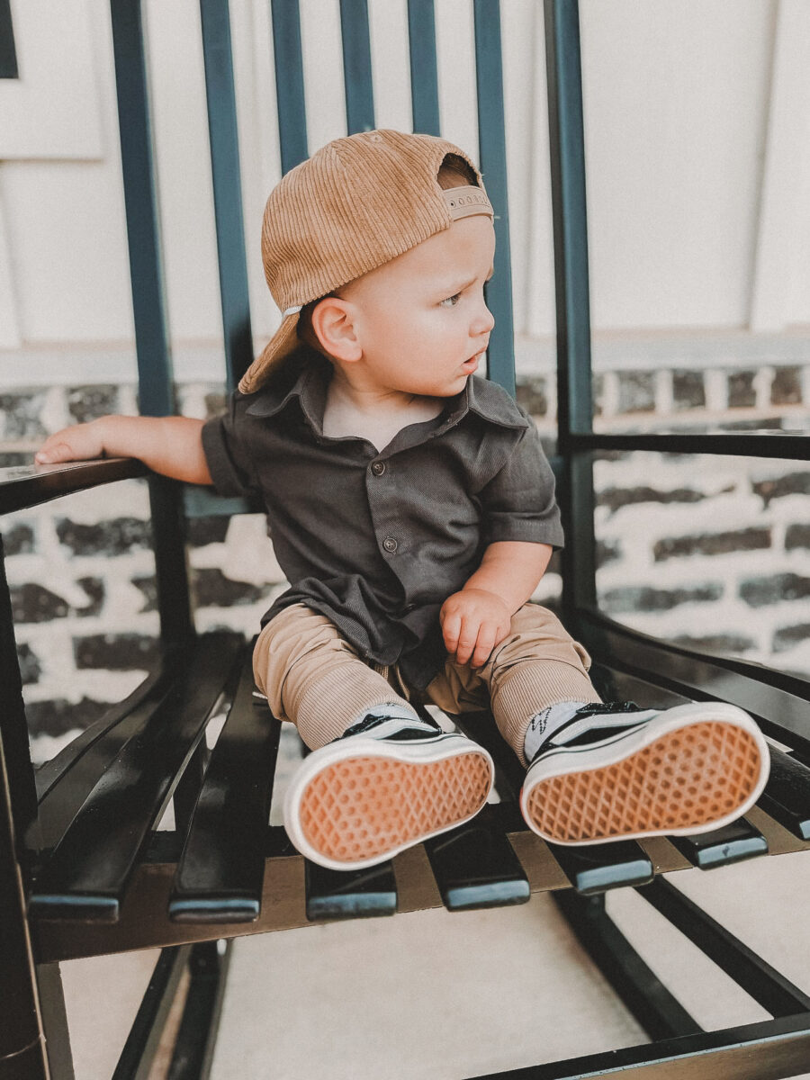 boy sitting on a chair while wearing a cute charcoal colored button up and beige hat