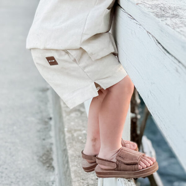 boy standing on a pier wearing a comfortable beige linen outfit with a leather patch by Rad toddler