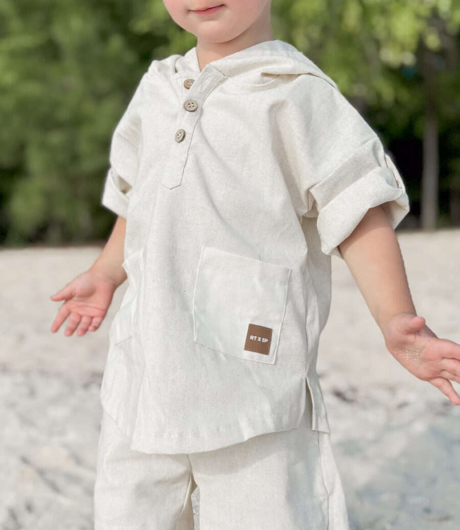 boy standing on a beach wearing a comfortable beige linen outfit with a leather patch by Rad toddler