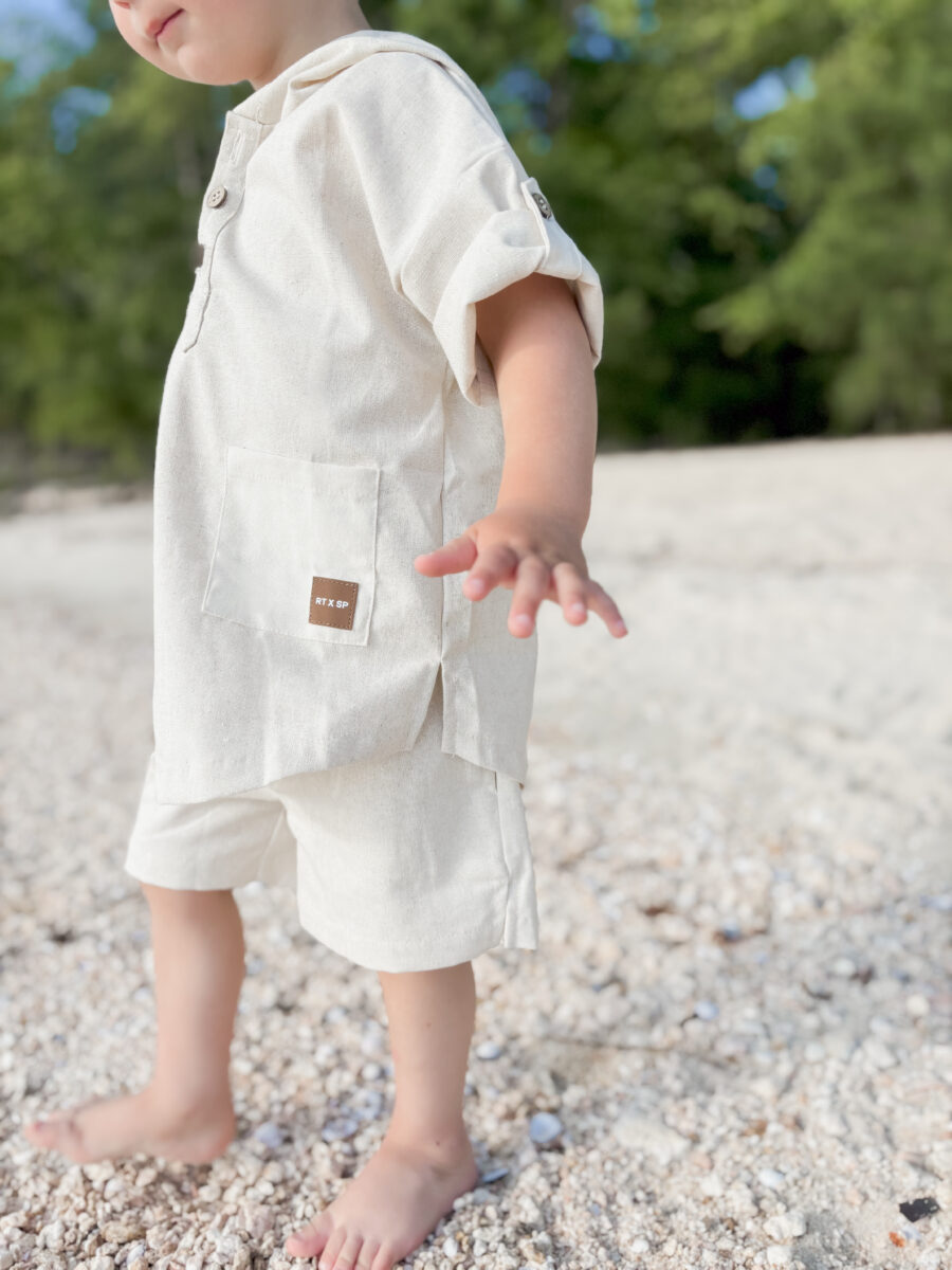 boy standing on a beach wearing a comfortable beige linen outfit with a leather patch by Rad toddler